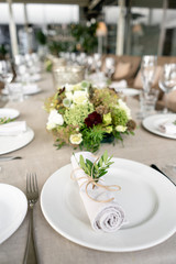 Neatly twisted into a tube dining room napkin decorated with a sprig of pistachio. Wedding Banquet or gala dinner. The chairs and table for guests, served with cutlery and crockery. party on terrace