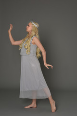 full length portrait of blonde girl wearing crow and grey dress, standing pose in side profile.  grey studio background.