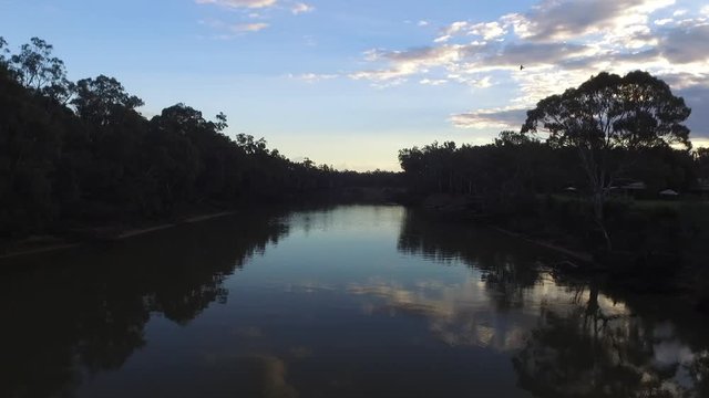 Drone aerial low down view travelling over The Murray River, sunset, clouds in reflection of water. Cadell New South Wales, Australia.