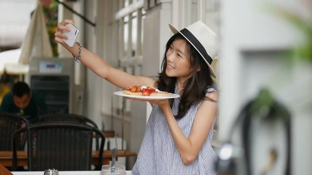 Beautiful asian woman taking selfies on a smartphone. Young asian girl take photo with pancake at cafe shop.