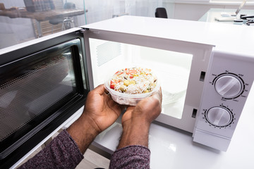 Man's Hand Heating Food In Microwave Oven
