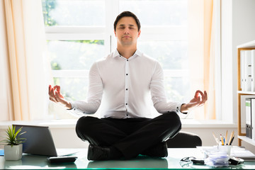 Businessman meditating in lotus position - obrazy, fototapety, plakaty