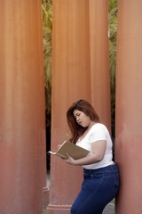 Portrait of Asian pretty smiley face fat woman pose and writing at a booklet on group of pole in the park.