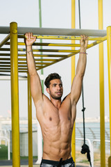 Obraz premium Young muscular athlete doing pushups on horizontal bar outdoor