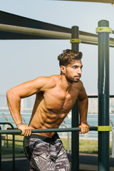 Portrait of a young arab sports man exercising with push ups exercise on horizontal baroutdoors in Dubai during summer time.