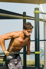 Portrait of a young arab sports man exercising with push ups exercise on horizontal baroutdoors in Dubai during summer time.