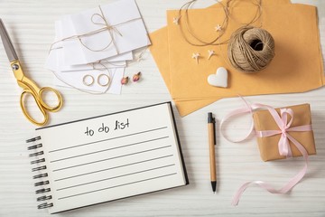 Flat lay and top view of to-do list and wedding invitations on a white wooden tabletop, blank space.