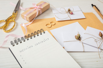 Flat lay and close up view of checklist and wedding invitations on a white wooden tabletop, blank...