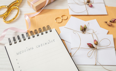 Flat lay and close up view of checklist and wedding invitations on a white wooden tabletop, blank...