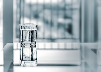 Close up purified fresh drink water with reflection on glass table in living room. Monochrome blurred background with copyspace.