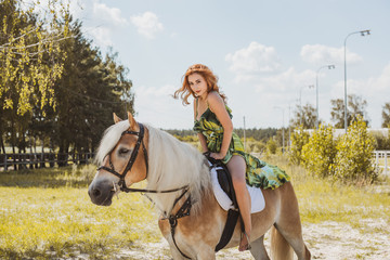 Fototapeta premium Nice red hair girl at countryside with a horse. A beautiful rider and horse. Artistic Photography at horse farm. Attractive girl riding on horse rural location at autumn 