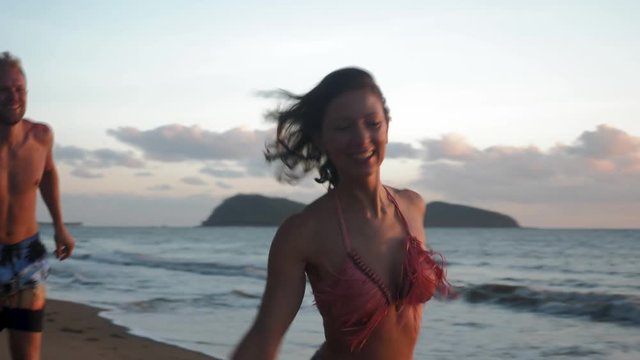 Young Bikini Woman Skips Along Beach at Sunrise with Young Man 