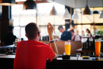 Blurred silhouette of a smoking man in a bar focus on a beer glass. Man drinks beer in bar alone after work. Smoking and drinking bad habits concept