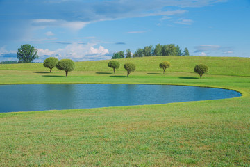 Sunny day, lake and meadow with blue sky. Treeas and clouds.