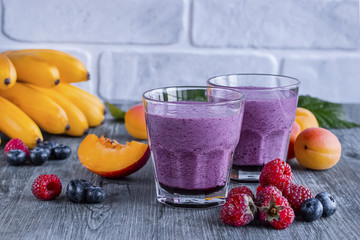 Homemade smoothies of fresh berries and fruits in glasses on gray wooden table.