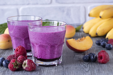 Homemade smoothies of fresh berries and fruits in glasses on gray wooden table.