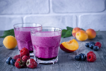 Homemade smoothies of fresh berries and fruits in glasses on gray wooden table.