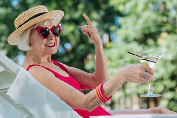 Modern grandmother. Modern beaming grandmother with bright red lips sunbathing near outdoor pool