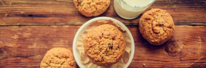 A close-up of a stack of pumpkin oat cookies on white parchment and gold swirl paper with golden raisins, cacao nibs and a glass of almond milk in the background.