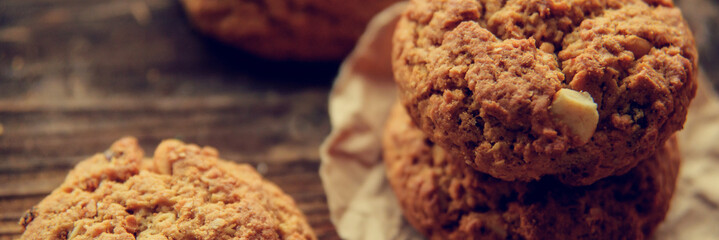 A close-up of a stack of pumpkin oat cookies on white parchment and gold swirl paper with golden raisins, cacao nibs and a glass of almond milk in the background.