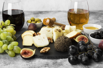 Snacks with wine - various types of cheeses, figs, nuts, honey, grapes on a gray background