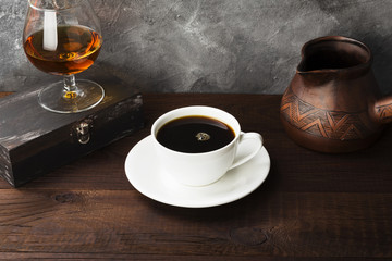 Coffee in white cup with cognac and clay cezve on wooden background