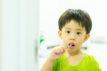 A boy brushes his teeth by himself in the restroom.