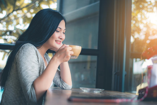 Beautiful attractive young Asian woman holding a cup of coffee or coffe in hand at cafe in the morning, vintage color tone. 