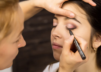 Make-up artist applying liquid eyeliner with brush to beautiful woman face. Make up in process