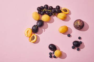 top view of fresh ripe sweet apricots, grapes, plums, blueberries and fig on purple background