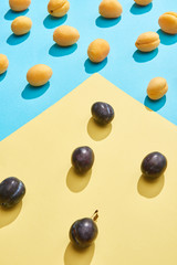 close-up view of fresh sweet plums and apricots on blue and yellow background