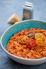 Bowl of tomato risotto topped with fresh sliced tomatoes, vertical shot, closeup