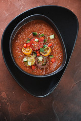 Tomato soup gazpacho served in a black bowl over rusty metal background, flatlay, vertical shot