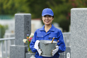 お墓の掃除をする作業服の女性