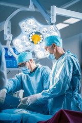 Shot In Operating Room of Two Surgeons During the Surgery Procedure Bending Over Patient with Instruments. Professional Doctors in Modern Hospital