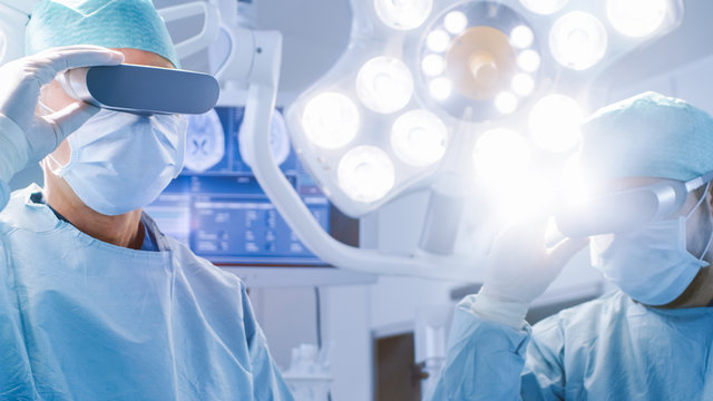 Surgeons Put on Augmented Reality Glasses to Perform State of the Art Surgery in High Tech Hospital. Doctors and Assistants Working in Operating Room.