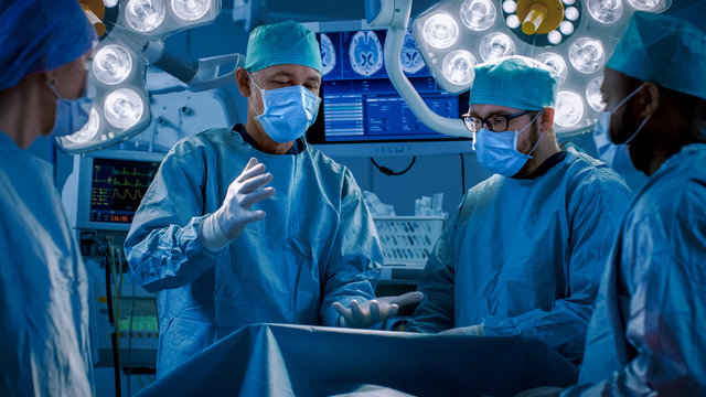 Diverse Team of Professional Doctors Performing Invasive Uses Augmented Reality Technology on a Patient in the Hospital Operating Room. Real Modern Hospital with Authentic Equipment.