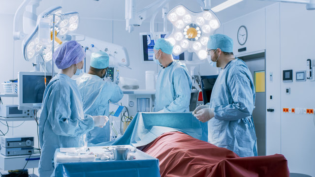Diverse Team of Professional surgeon, Assistants and Nurses Performing Invasive Surgery on a Patient in the Hospital Operating Room. Surgeons Talk and Use Instruments. Real Modern Hospital