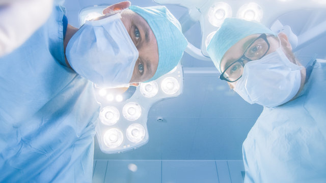 Low Angle Shot POV Patient View: Two Professional Surgeons Holding Surgical Instruments Starting Surgery.