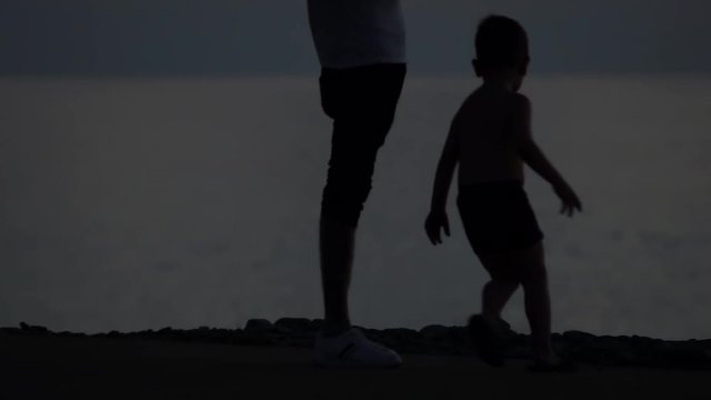 silhouette of a young boy running around his father. vacation father and son at sea. child pampering and mischief