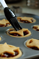 Brushing egg wash onto mince pies in a baking tray preparing them to be cooked in the oven