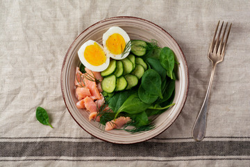 Scandinavian salad with smoked pink salmon, spinach, cucumber and chicken egg in gray ceramic dish. Top view. © kasia2003
