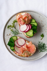 Sandwiches with smoked pink salmon, radish, cucumber and cream cheese on gray ceramic plate and textile background. Traditional Scandinavian toast. Top view.