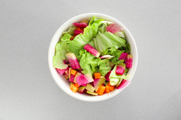 Fresh salad with sliced radish and lettuce in bowl on light background, top view
