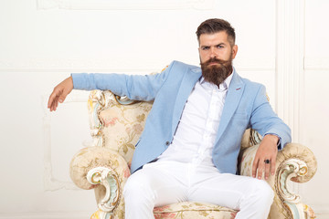 Successful young bearded elegant businessman in suit with perfect hairstyle indoors, relaxing, sits...