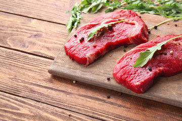 Raw meat with spices and arugula on wooden background