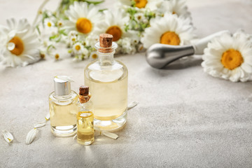 Fototapeta na wymiar Bottles with essential oil and chamomile flowers on table