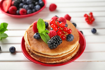 Plate with tasty pancakes and berries on wooden table