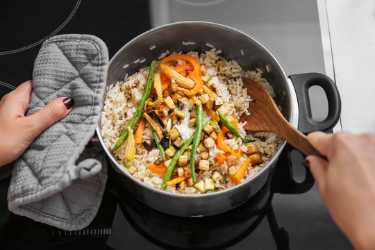 Woman cooking tasty rice with vegetables in kitchen