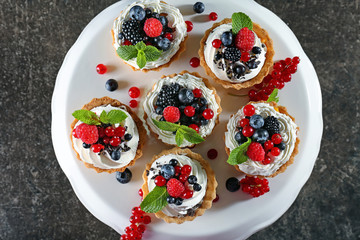 Tasty tartlets with whipped cream and berries on dessert stand, top view